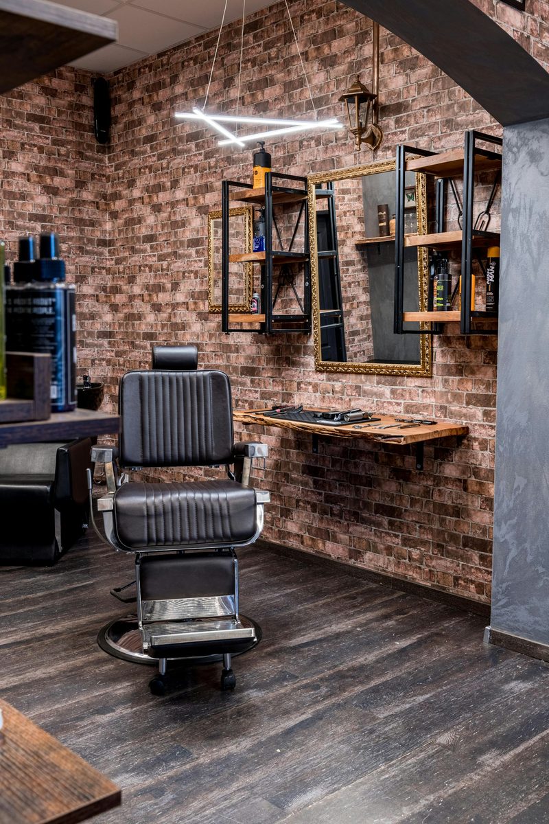 An empty barber chair beside a brick wall, with clippers and combs laid out on a wood shelf, for atmosphere - not a photo of any shop listed above