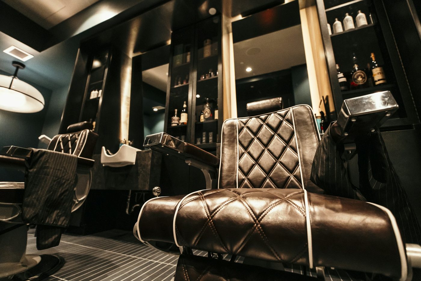Two empty leather barber chairs and a shampoo basin in a dark barbershop, for atmosphere - not a photo of any shop listed below